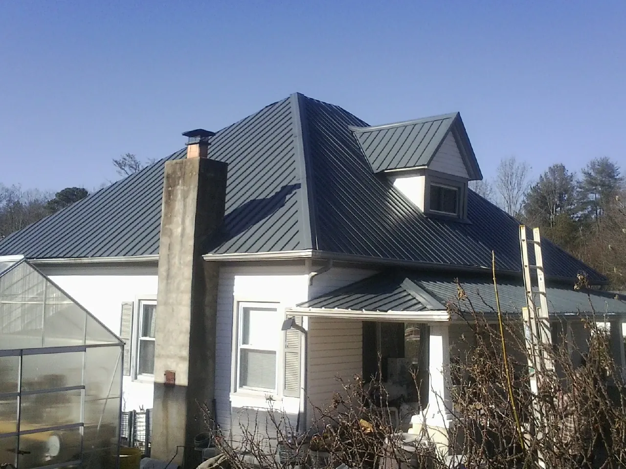 Dark blue standing seam metal roof on a white farmhouse with dormer — Slate & Tile Roof Repair by Roofing Brothers in Shelby