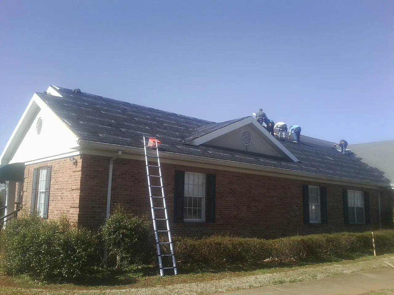 Crew tearing shingles off a brick ranch roof with a ladder set — Emergency Roof Repair work by our crew in Shelby