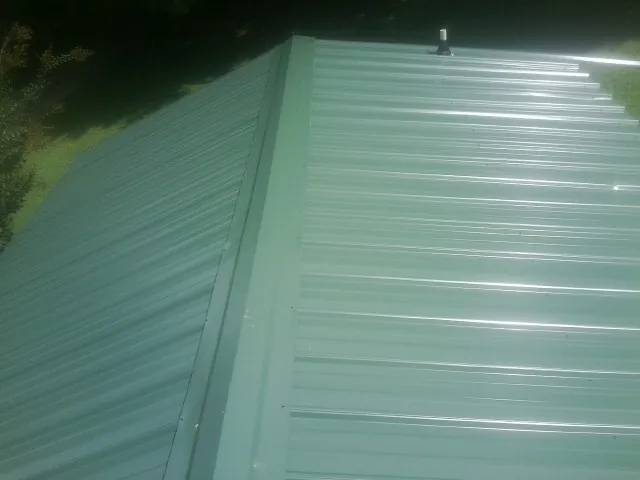 New green metal panels meeting at the ridge of a roof — Flat Roof Repair work by our crew in Shelby